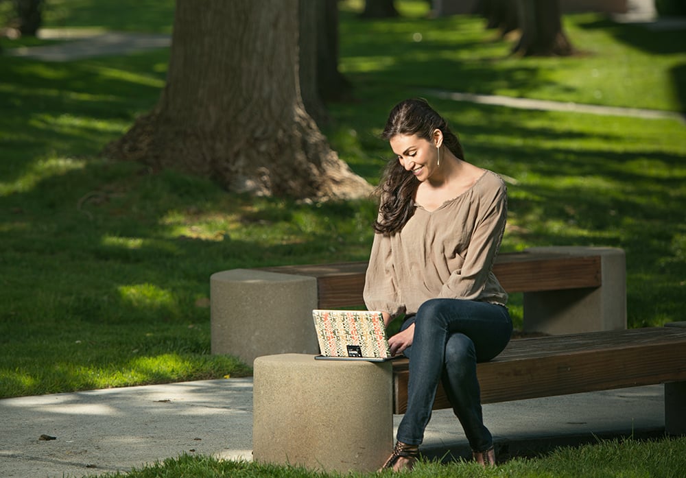 Woman sitting on a bench in a park using her laptop